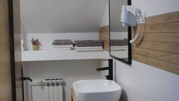 Un baño con un lavamanos blanco, un perchero con toallas dobladas, un espejo y un secador de pelo montado en la pared.