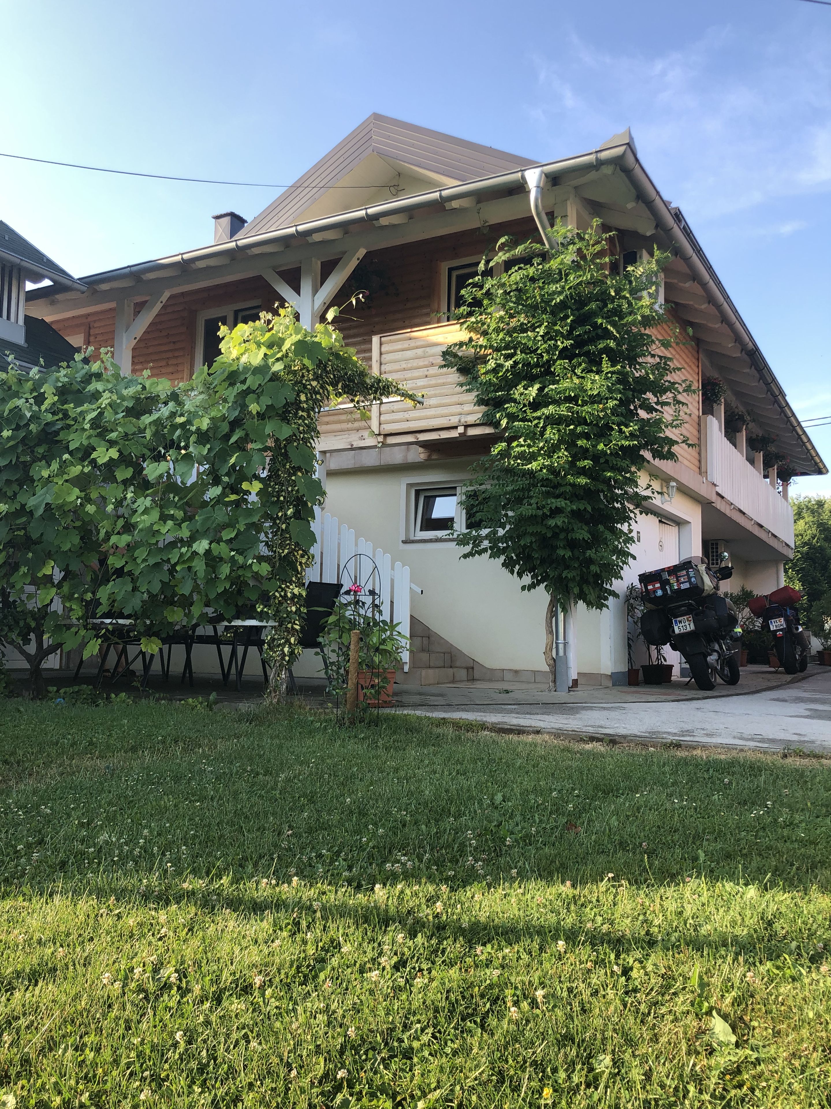 A two-story house with a sloped roof, a front porch, and a small front yard with grass and a tree.