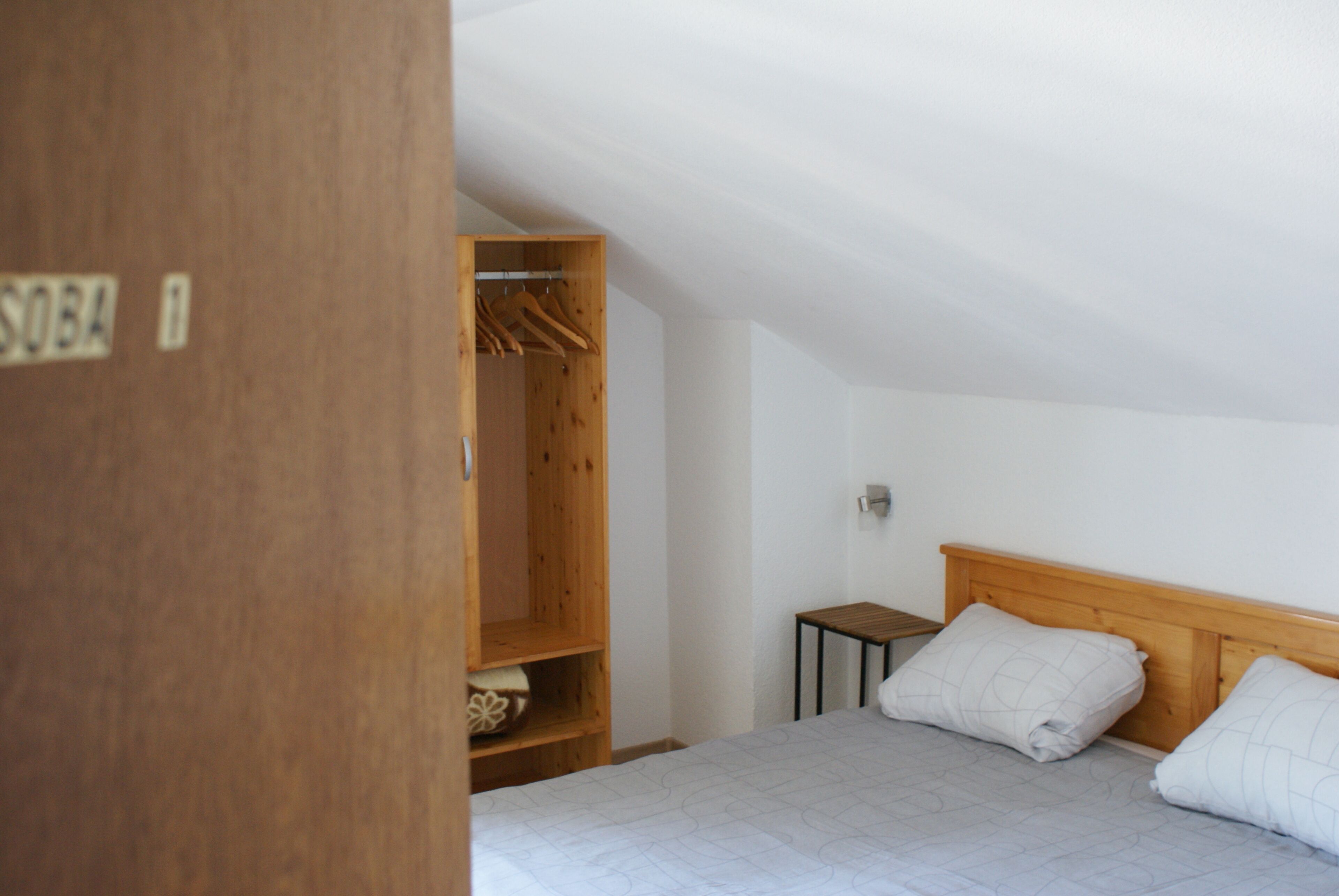 A bedroom with a bed, a wooden wardrobe, and a small bedside table.