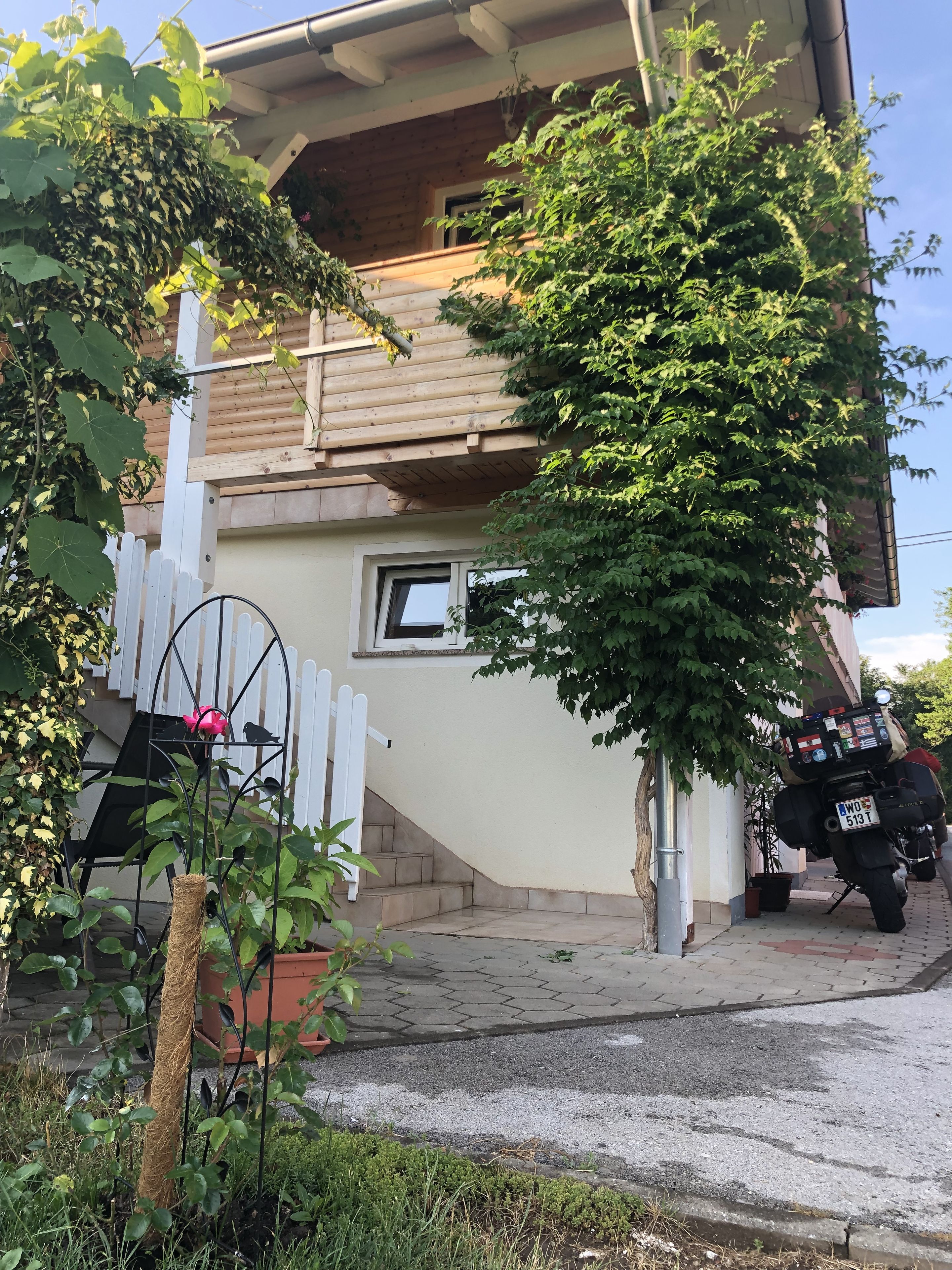 Una casa di legno con un balcone, un recinto in legno bianco e una motocicletta parcheggiata davanti.