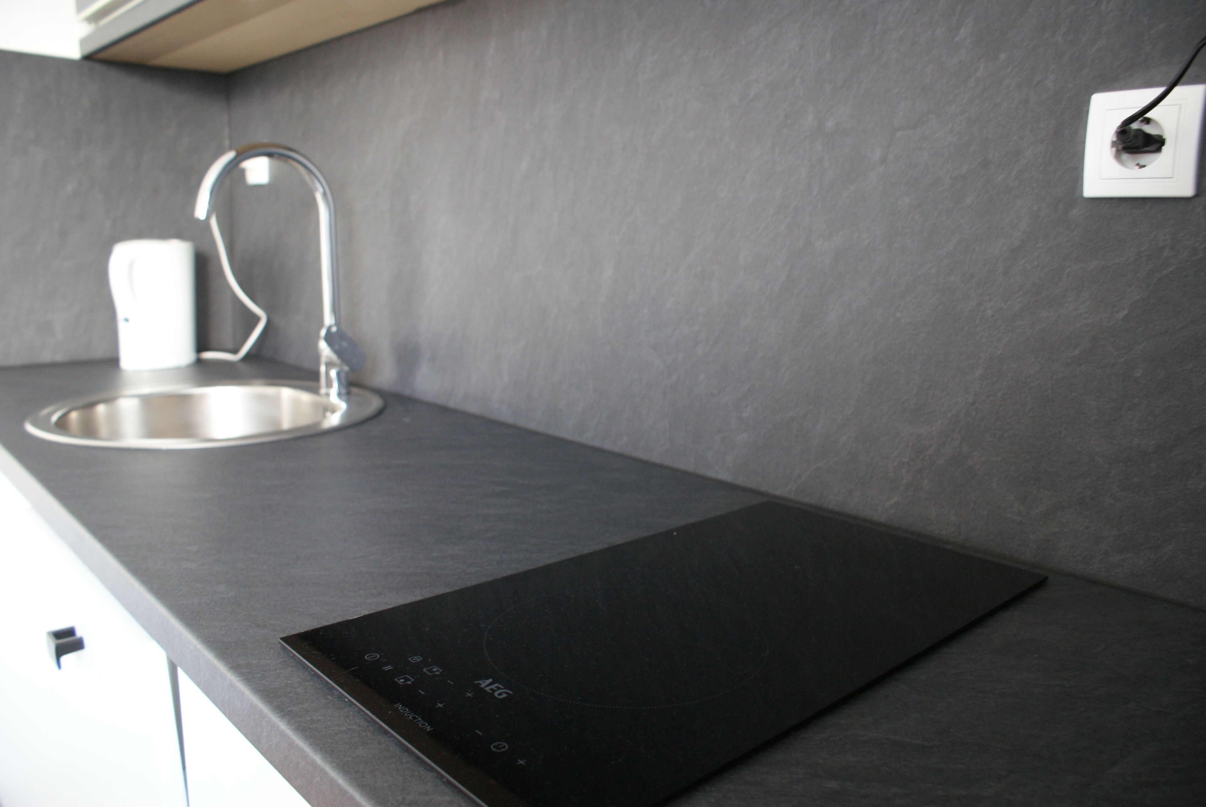 Una cucina moderna con un lavandino in acciaio inossidabile, un piano cottura a induzione nero e una tazza bianca sul ripiano.