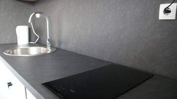 Una cucina moderna con un lavandino in acciaio inossidabile, un piano cottura a induzione nero e una tazza bianca sul ripiano.