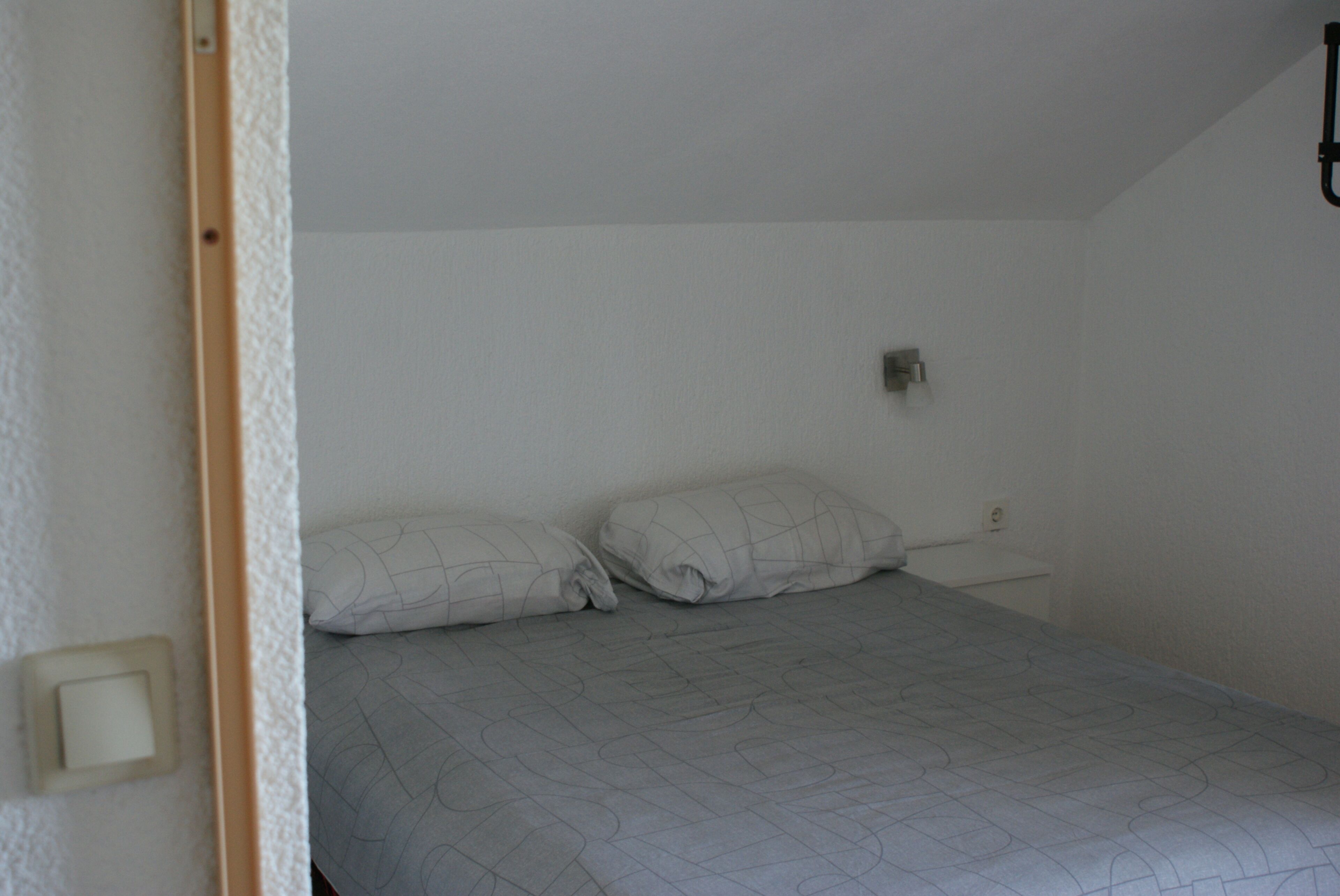 Una cama individual con una colcha estampada, una mesita de noche y un aplique de pared.