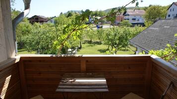 Una terraza de madera con una mesa y sillas, con vistas a un jardín con árboles y casas al fondo.