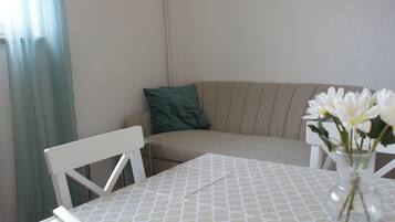 Una habitación pequeña y acogedora con una mesa, una silla, un sofá y un jarrón con flores.