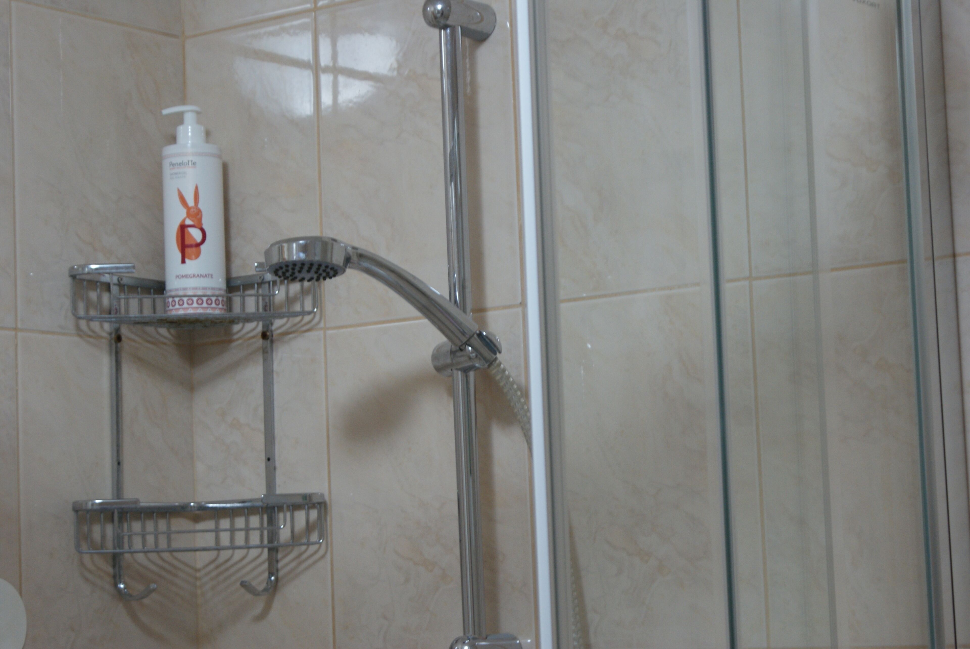 A bathroom with a shower, a hand dryer, and a soap dispenser on a shelf.
