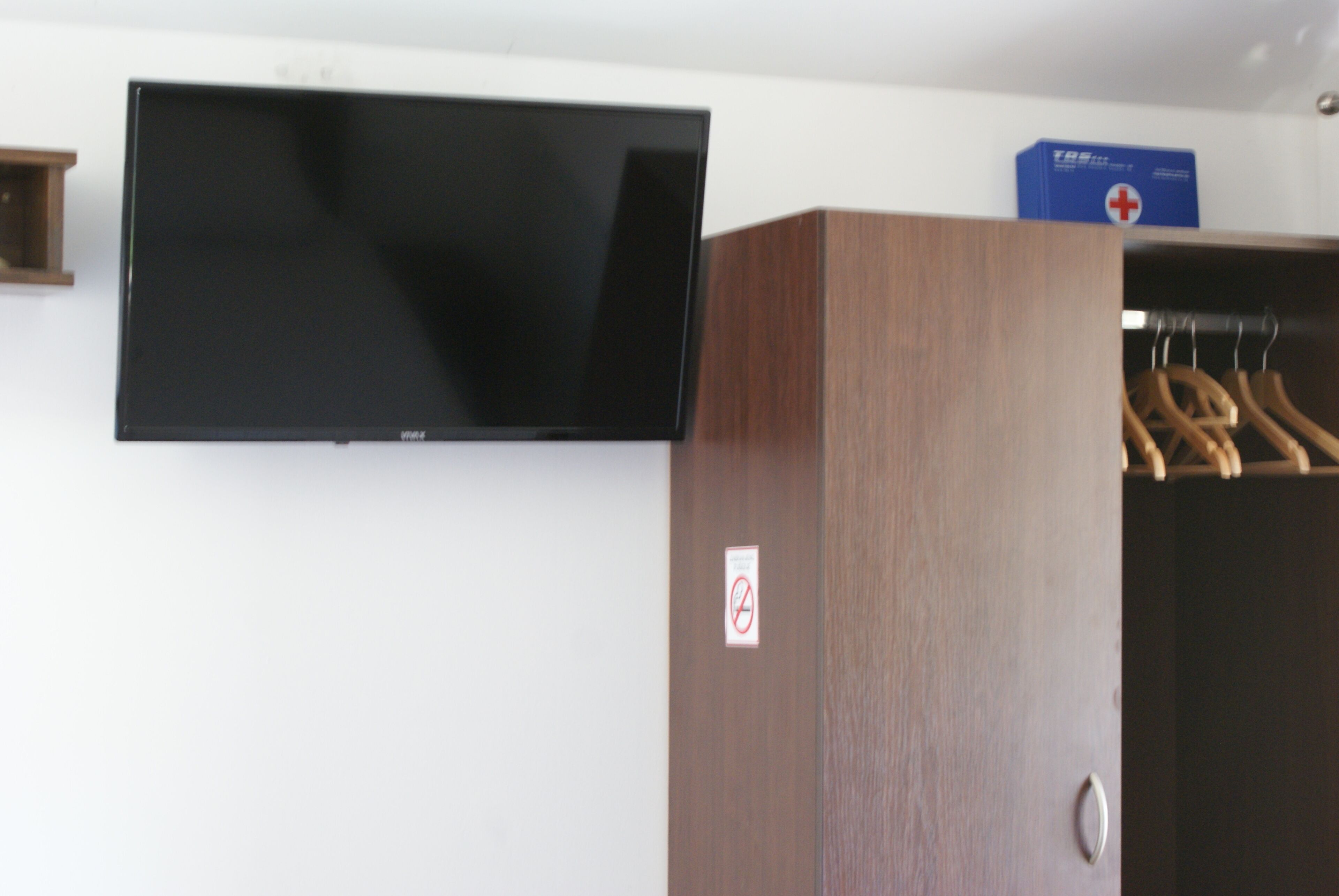 Una habitación con televisión de pantalla plana en la pared, un armario de madera y una caja azul con una cruz roja.