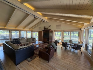 A spacious living room with a high ceiling, large windows, and a fireplace.