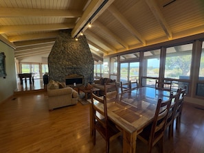 A spacious living area with a stone fireplace, wooden ceiling, and large windows offering a view.
