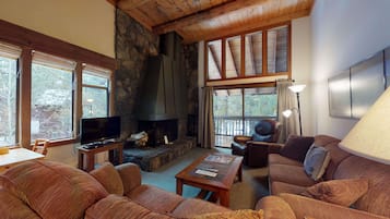 A cozy living room with a stone fireplace, comfortable seating, and large windows.
