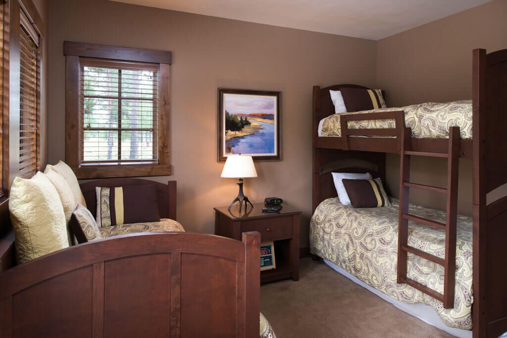 A room with a bunk bed, a desk with a lamp, a window with blinds, and a painting on the wall.