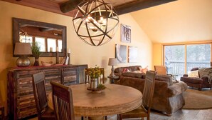 A cozy living room with a round wooden dining table, two brown leather sofas, and a large window providing natural light. - Charming Lodge Condo with Access to The Cove (Sunriver)