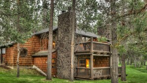 A log cabin with a stone chimney, wooden balconies, and a surrounding forest. - Charming Lodge Condo with Access to The Cove (Sunriver)
