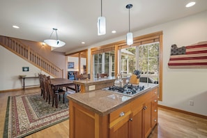 A kitchen with a central island, wooden cabinets, a gas stove, and pendant lights.