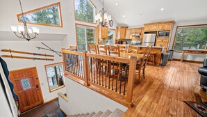 A spacious kitchen with wooden cabinets, a dining area with a wooden table and chairs, and a staircase with a wooden railing. - Reverse-Living Retreat with Access to Exclusive Golf (Sunriver)
