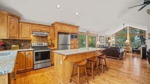 A spacious kitchen with wooden cabinets, stainless steel appliances, and a large island with bar stools. - Reverse-Living Retreat with Access to Exclusive Golf (Sunriver)