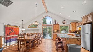 A spacious kitchen with wooden cabinets, a stainless steel refrigerator, and a large island with bar stools. - Reverse-Living Retreat with Access to Exclusive Golf (Sunriver)