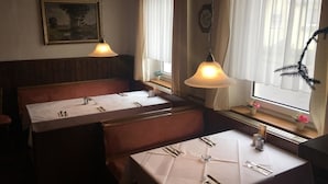 A restaurant with booths and tables, wooden paneling, a painting on the wall, and a window with curtains.