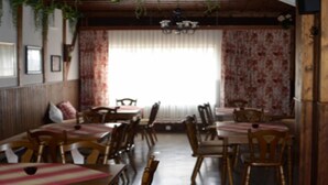 A restaurant with wooden tables and chairs, a large window with floral curtains, and a chandelier.