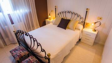 A neatly made bed with a headboard, two bedside tables with lamps, and a bench with a floral pattern.