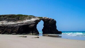 A natural rock arch formation on a beach with clear blue skies. - Casa Brais (Barreiros)