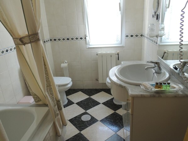 Un baño con piso a cuadros, una bañera, un inodoro, un lavamanos y una ventana.