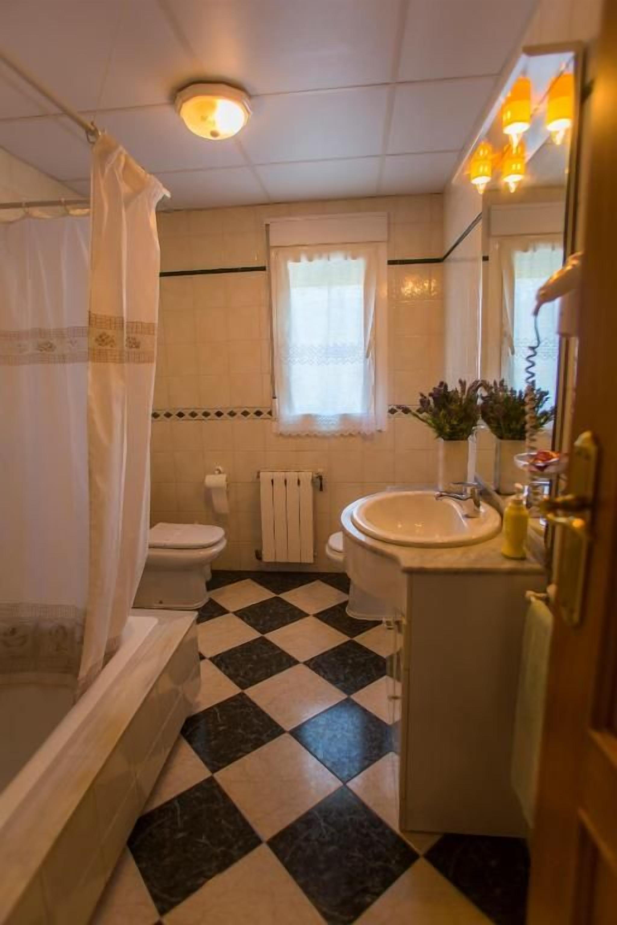 A bathroom with a checkered floor, a toilet, a sink, and a shower area.