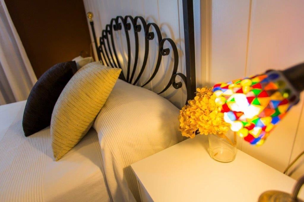 Un lit avec une tête de lit, une table de chevet ornée d’un vase de fleurs jaunes et un objet coloré posé sur la table.