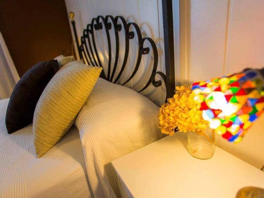 A bed with a headboard, a bedside table with a vase of yellow flowers, and a colorful object on the table.