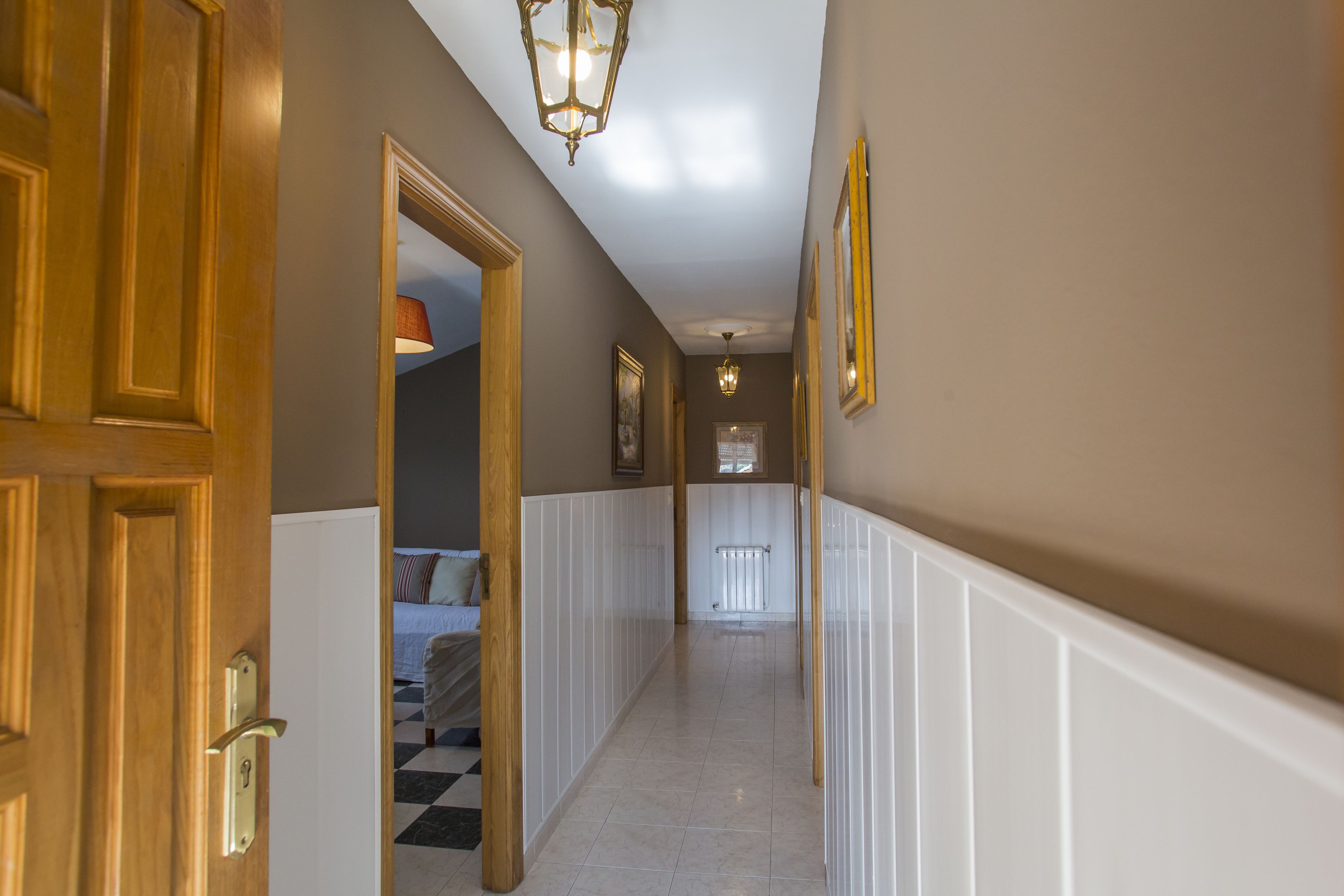 A hallway with wooden doors, white wainscoting, and a checkered floor.
