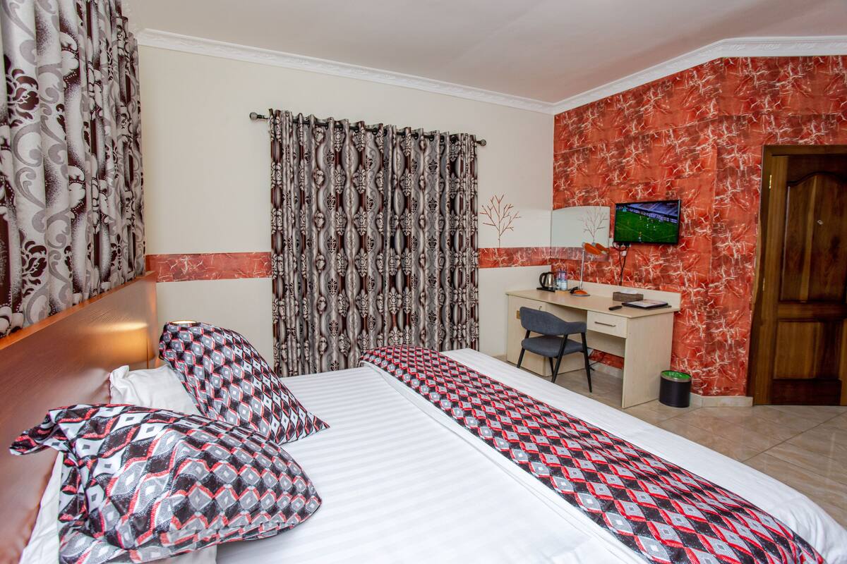 A hotel room with a bed, a desk, a chair, a TV, and a door.