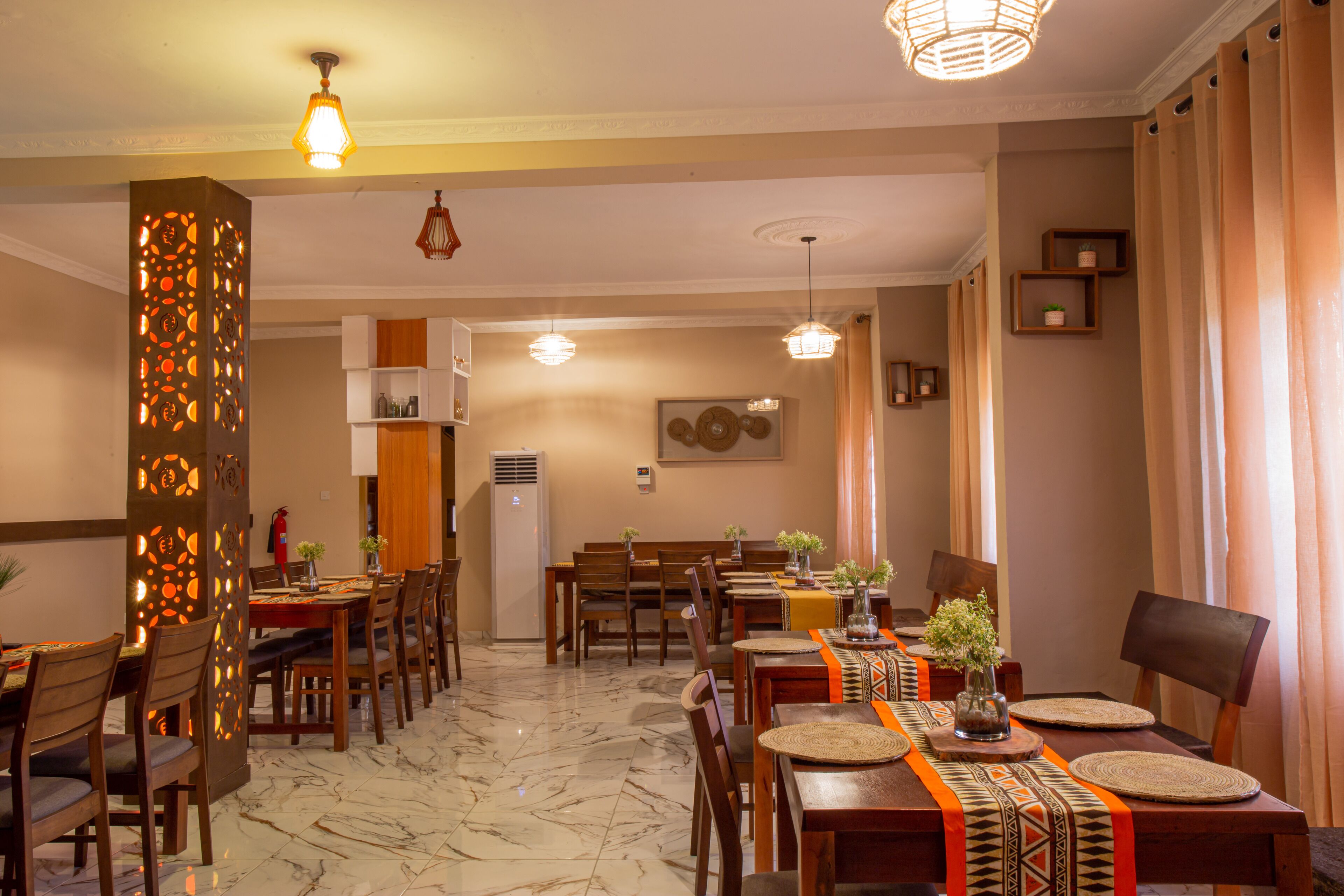 Un comedor de hotel con varias mesas y sillas, un muro decorativo y luces en el techo.