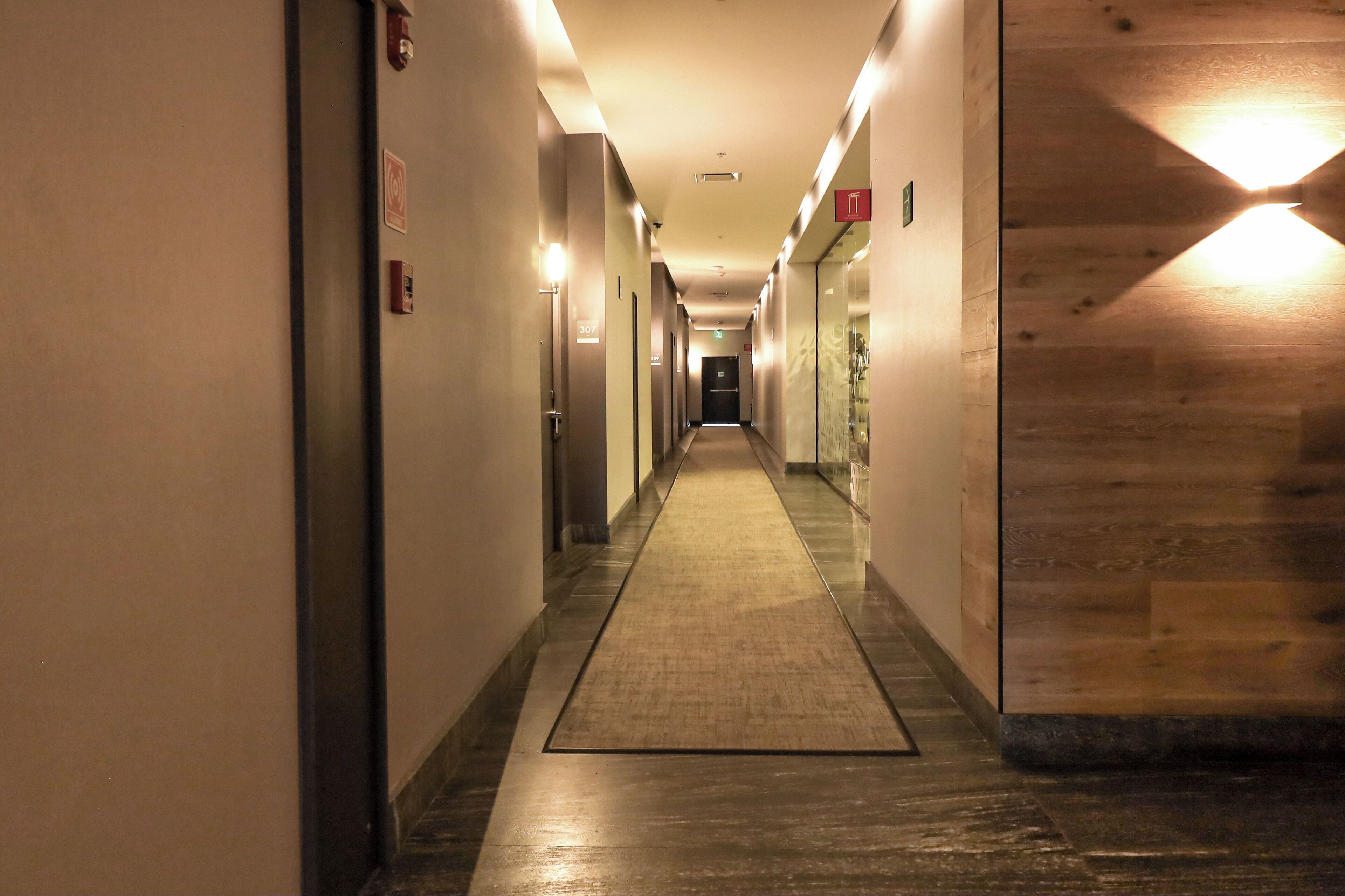 Un pasillo de hotel con piso alfombrado, paneles de madera en una pared y varias puertas a lo largo del corredor.