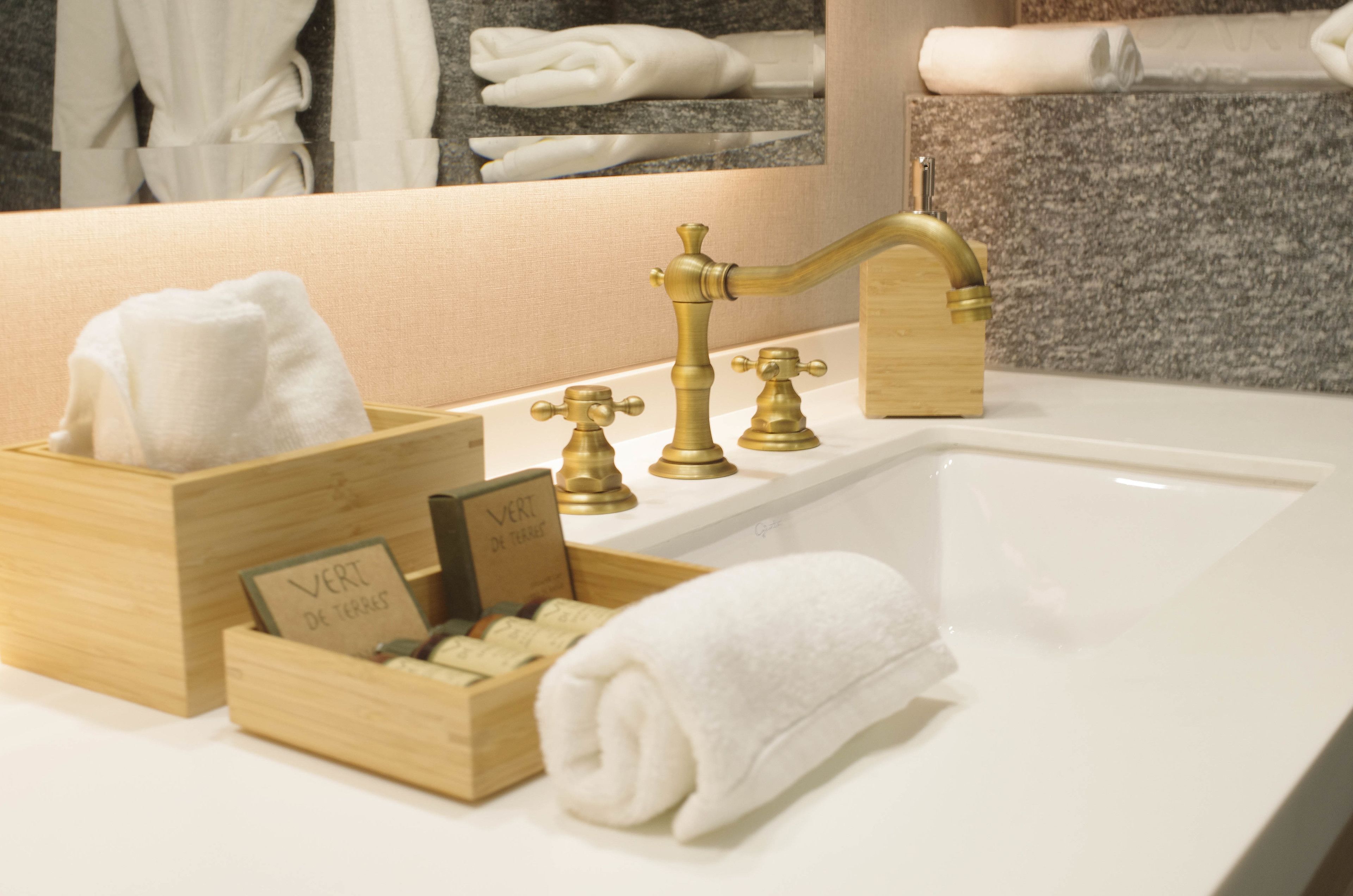 A bathroom with a white sink, gold faucets, and a wooden box with toiletries.