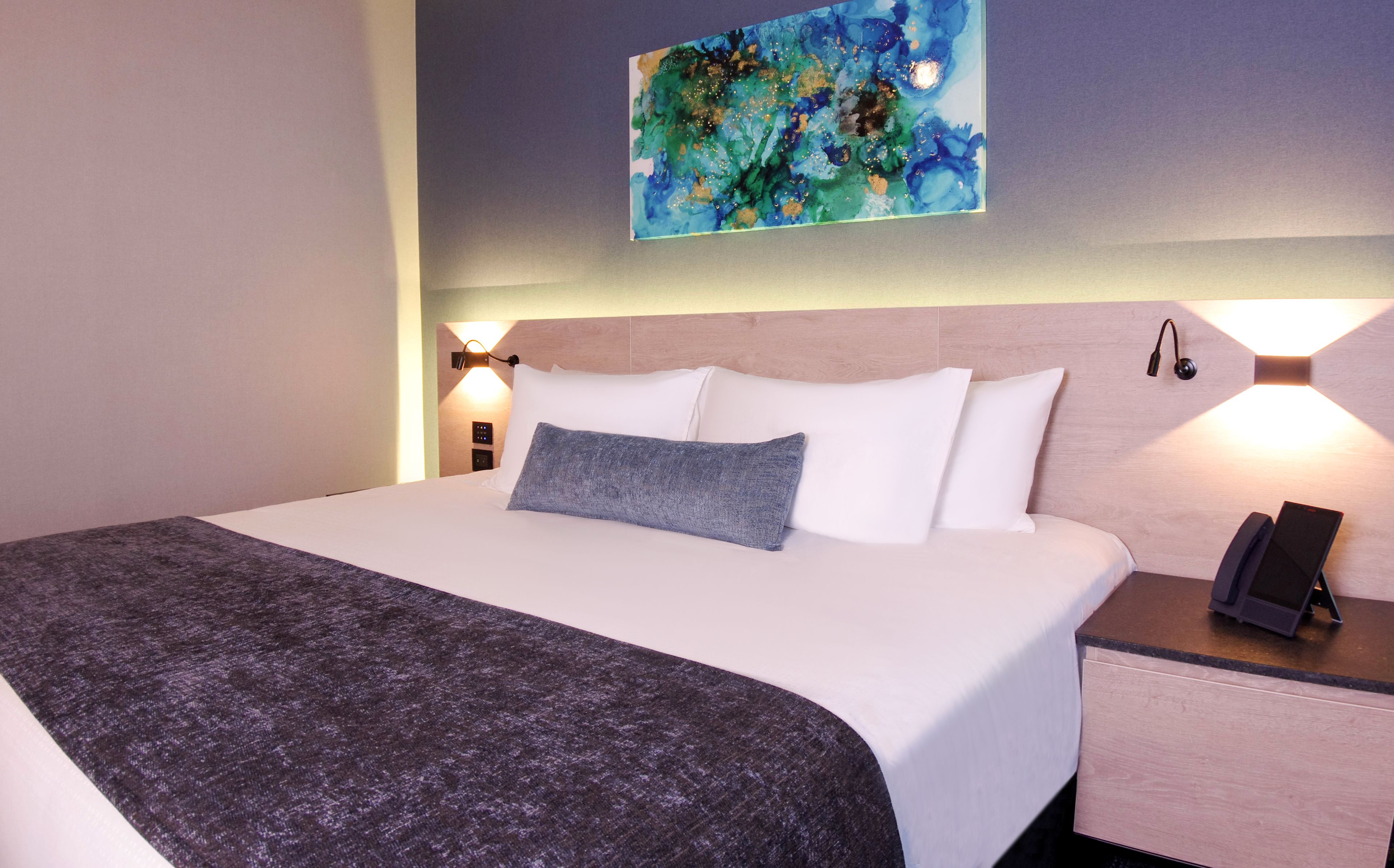 Een hotelkamer met een groot bed, een nachtkastje met een telefoon en een schilderij aan de muur.