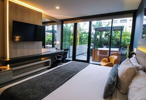 A modern hotel room with a large bed, a desk, a flat-screen TV, and a view of the outdoors.