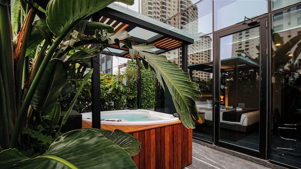 Un jacuzzi en un entorno moderno al aire libre, con grandes hojas verdes y una puerta de vidrio que da a una habitación.