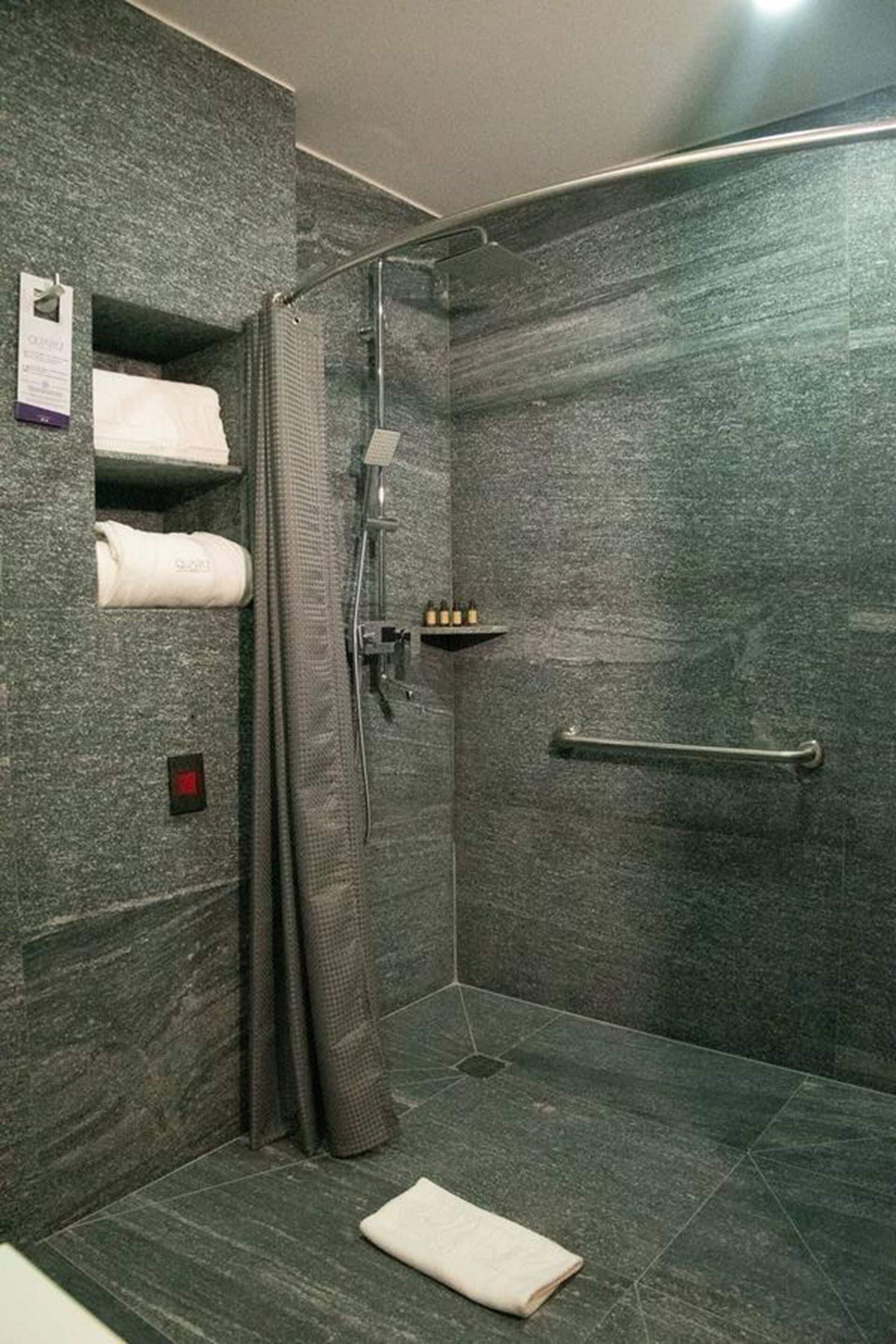 A modern shower room with a glass door, a towel rack, and a handrail.
