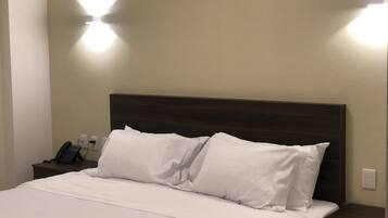 A hotel room with a bed, white bedding, a dark headboard, and two wall-mounted light fixtures.