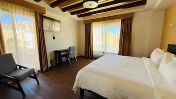 A hotel room with a large bed, a desk, and a chair. There are curtains on the windows, and a TV mounted on the wall.