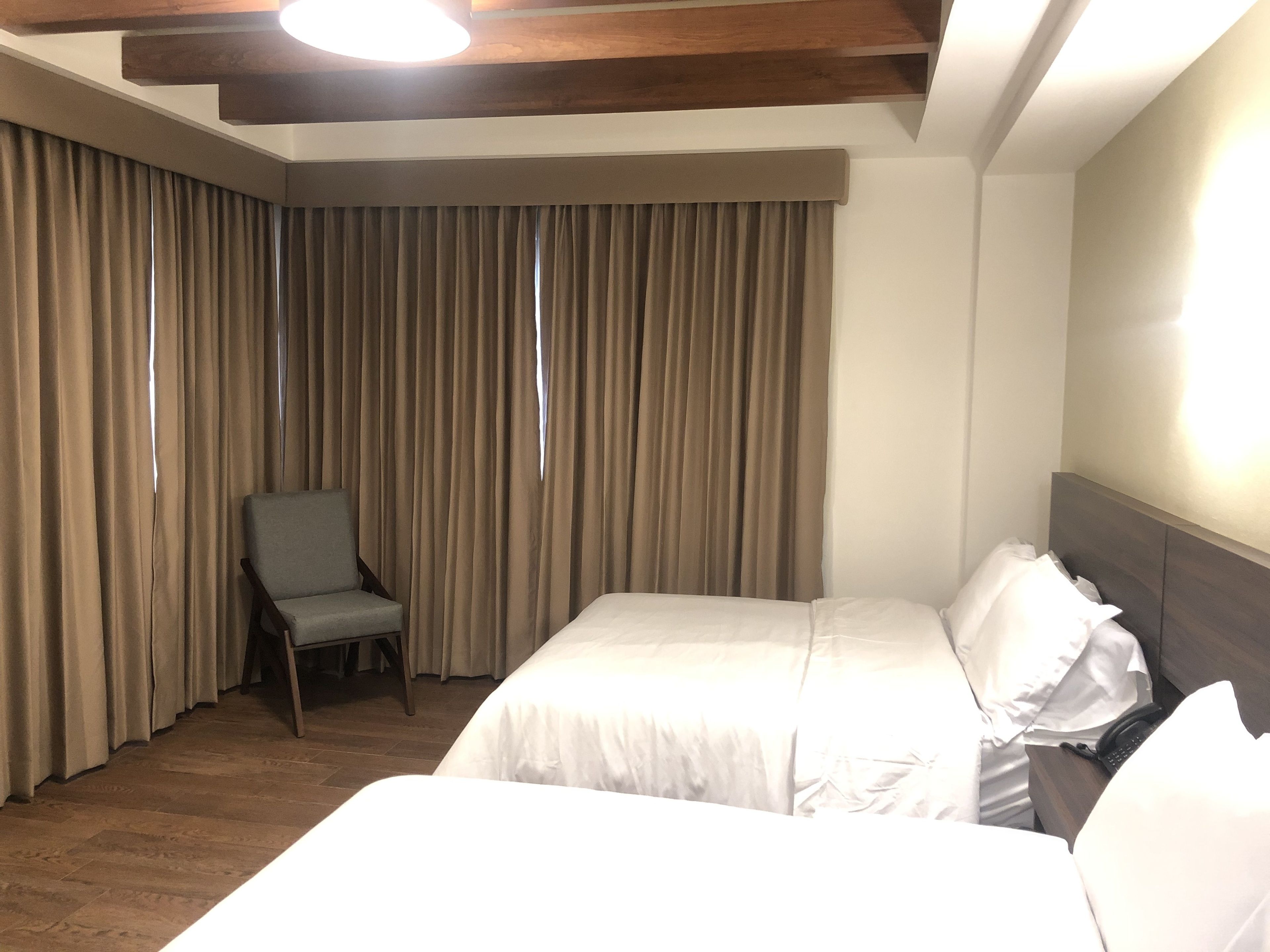 Una habitación de hotel con una cama grande, una silla y una ventana con cortinas.