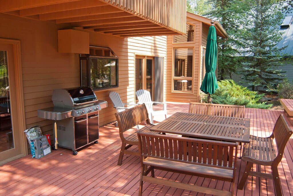 Une terrasse en bois avec un barbecue, des chaises et une table.