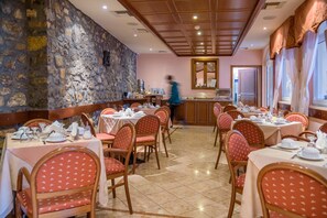 Restaurante con paredes de piedra, techo de madera y sillas tapizadas en rojo. Las mesas están dispuestas con manteles blancos y platos.