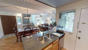 A modern kitchen with granite countertops, stainless steel sink, and wooden cabinets. There is a dining area with a wooden table and chairs, and a staircase leading to another level.