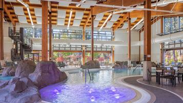 An indoor swimming pool with a hot tub, rock formations, and a staircase leading to upper levels.
