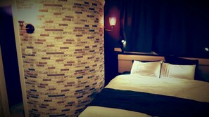 Hotellihuone, jossa on tiiliseinä, valkoisilla lakanoilla varustettu sänky ja yöpöytä, jossa on lamppu.