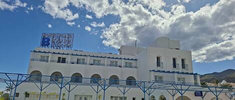 A hotel with a sign reading "HOTEL PLAZA BOMA," featuring a white facade, multiple balconies, and a covered outdoor seating area with potted plants.