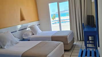 Een hotelkamer met twee bedden, een bureau en uitzicht op het strand.