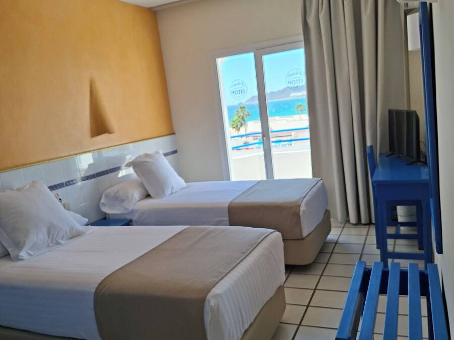 A hotel room with two beds, a desk, and a view of the beach.