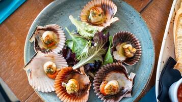 A plate of scallops with a garnish of greens and a side of bread.